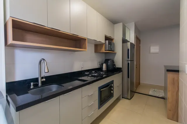 Cozinha planejada em corredor, com armários off-white, nichos de madeira e bancada preta com cuba embutida
